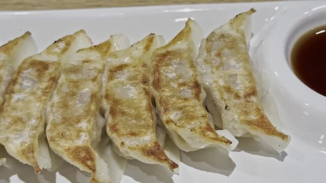 Close-up of golden fried gyoza served with savory dipping sauce, showcasing a crispy wrapper and juicy filling in an appetizing Japanese-style appetizer.