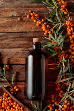 Antique dark glass pharmacy bottle filled with sea buckthorn oil with fresh branches of bright orange berries on a wooden background.