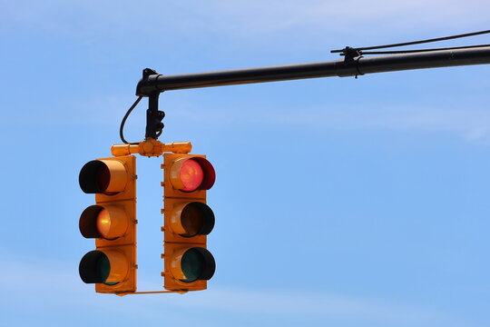Close-up of an yellow traffic light suspended from a black metal pole against a clear blue sky, showing illuminated red and yellow signals. New York, USA