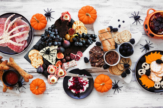 Halloween theme grazing table scene against a white wood background. Spooky charcuterie boards of meat and cheese appetizers. Top down view.