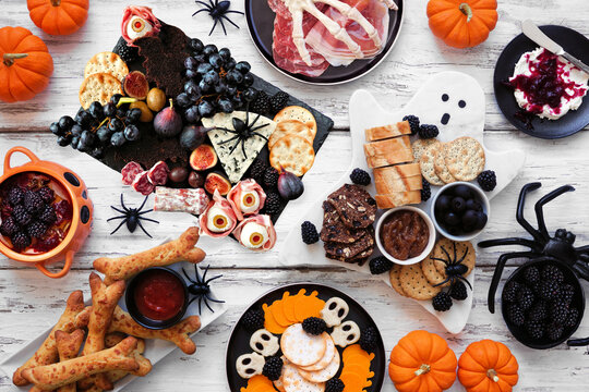 Halloween theme grazing table scene against a white wood background. Spooky charcuterie boards of meat and cheese appetizers. Overhead view.