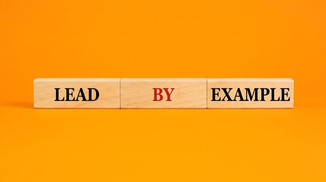 Lead by example text on wooden blocks, leadership concept on orange background, business management and role model inspiration