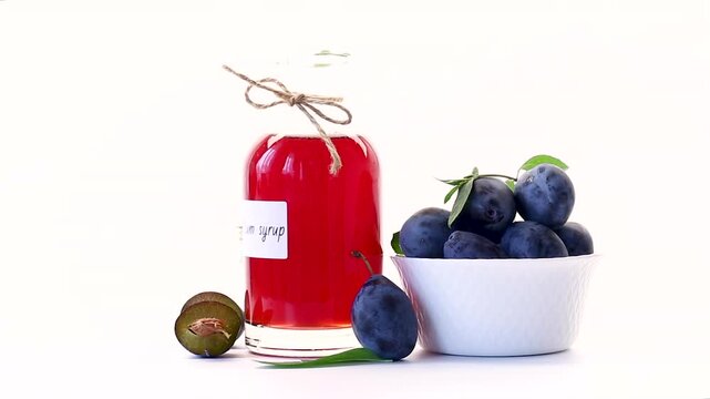 Red plum syrup in bottle with fresh plums on white background