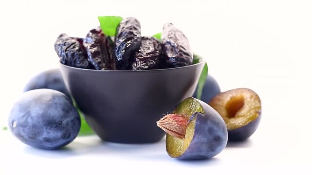 Dark dried plums in bowl with fruit on white background