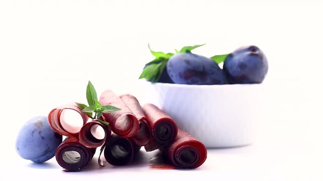 Natural plum fruit leather rolls with fresh plums on white background