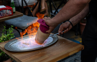 Fototapeta premium Istanbul,turkey,august 2, 2025. Chef dramatically opening a flaming testi kebab clay pot on a heated salt tray in a turkish restaurant, culinary performance