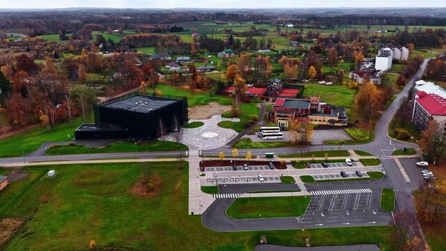 Aerial view of the modern Vidzeme Concert Hall surrounded by autumn trees, green lawns, and parking areas in Cesis, Cesis Municipality, Latvia.