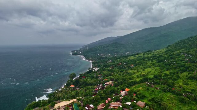 Aerial view of Amed Beach with lush green hills and coastal vegetation along the shoreline in Bali, Indonesia.
