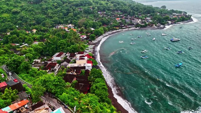 Aerial view of Amed Beach with traditional fishing boats anchored in turquoise waters along the lush green coastline of Bali, Indonesia.