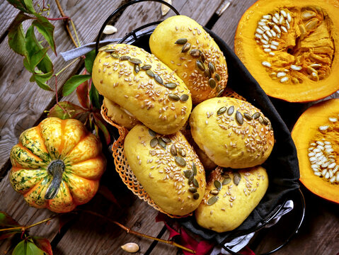 A basket of pumpkin seed-topped bread rolls is next to halved pumpkins and a small decorative pumpkin.