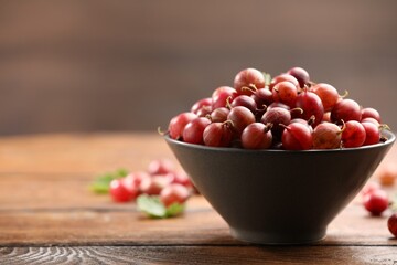 Fresh red gooseberries in bowl on wooden table, closeup. Space for text © New Africa