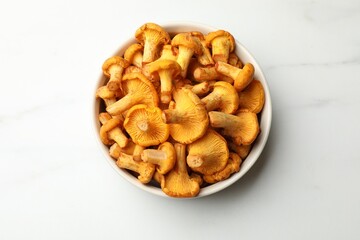 Fototapeta premium Golden chanterelle mushrooms in bowl on white marble table, top view