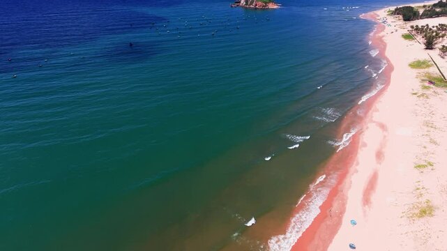 Waves crash on the sandy beach in Hoa Thang, Lam Dong. People gather under umbrellas, enjoying the sun. The sun shines brightly over the water. A stunning ocean view showcases the beauty of the area.