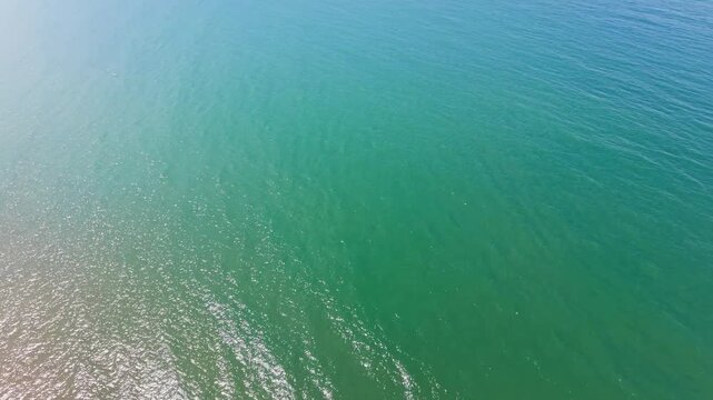 The camera shows the coastline of Hoa Thang in Lam Dong. Waves crash on the shore. The ocean spreads wide under the bright sky. The landscape shifts from land to sea.