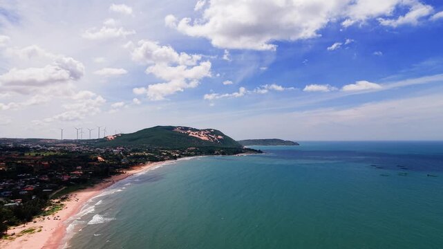 Aerial views show the coastline of Hoa Thang in Lam Dong. The sun shines brightly over the sand and water. Waves crash gently against the shore. People enjoy the beach and nature.