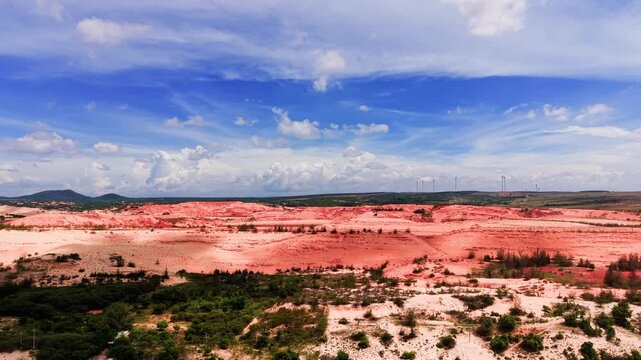 The wide landscape of Hoa Thang in Lam Dong. The sun shines brightly as the land features red earth, greenery, and clouds in a blue sky.