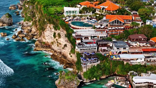 Aerial view of Uluwatu Beach resort featuring cliffside buildings, swimming pool, and rocky coastline overlooking the ocean in South Kuta, Bali, Indonesia.