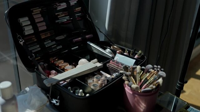 Makeup artist kit open with palettes lipsticks and a pot of brushes beside a ring light