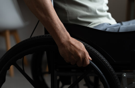 Close-up of an older adult hand gripping a wheelchair wheel at home, highlighting mobility, disability, independence, accessibility, rehabilitation, strength and daily adaptive living.