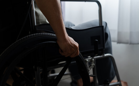 Close-up rear view of an older adult gripping a manual wheelchair wheel indoors, highlighting disability equipment, personal mobility, self-reliance, accessibility and independent movement.