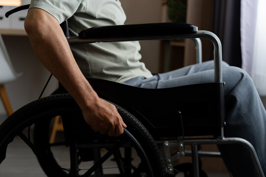 Close-up of a senior man's hand pushing a manual wheelchair wheel at home, representing mobility, disability, independence, accessibility, rehabilitation and adaptive daily living.