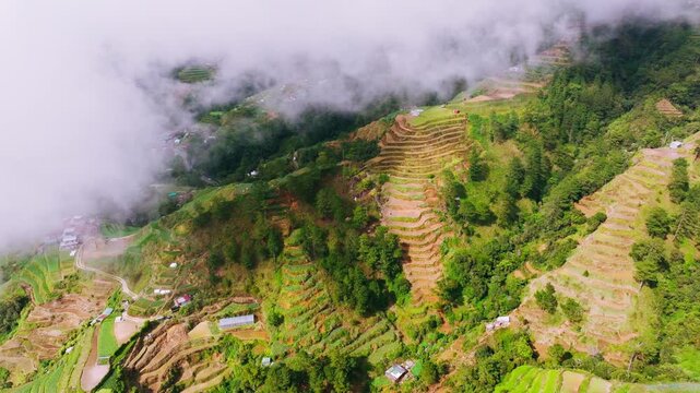 Drone turns left above terraced farms, drifting clouds in Benguet, Philippines
