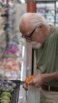An elderly man is shopping in a grocery store, focusing on selecting fresh vegetables during his visit.