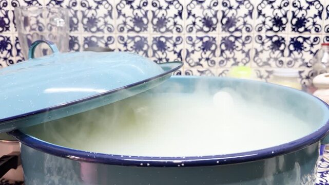 Hot steam rises from traditional blue enamel pot with boiling paste on classic kitchen stove