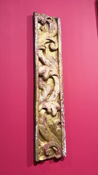 Baroque carved decorative panel with aged gilded floral scrollwork mounted on pink wall, vertical