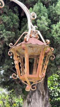 Rusty vintage lantern hanging outdoors with trees in background, daylight scene