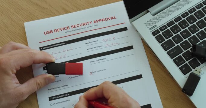Person holding a USB flash drive over a security approval form beside a laptop, representing device authorization, cybersecurity and secure data access.