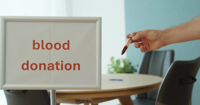 Person holding a blood sample next to a blood donation sign, representing voluntary donation, healthcare, lifesaving support and medical blood supply.