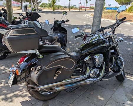 Vista lateral de moto cruiser Kawasaki Vulcan 900 Classic con maletas y ba&uacute;l trasero de cuero de est&eacute;tica custom, estacionada en Madrid, Espa&ntilde;a, 19 de junio de 2026	