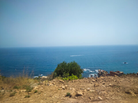 Vast Mediterranean sea view from a rugged rocky cliffside featuring deep blue water bright sunlight and a distant white boat on the clear horizon line