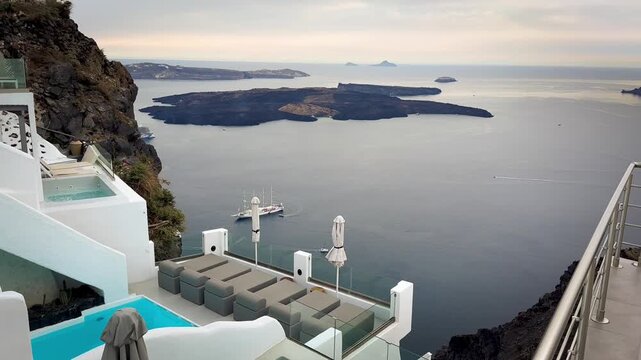Serene wide shot of a pristine cliff-edge luxury pool deck in Imerovigli, Santorini, with whitewashed modern architecture, infinity pools, and lounge beds overlooking Skaros Rock during sunset