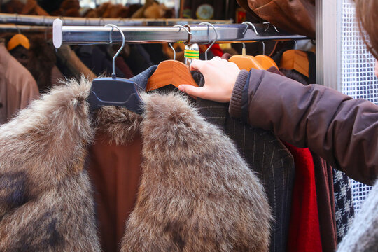 Hand of a customer browsing vintage clothes and fur coat on a rack at an outdoor street market