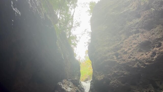 Waterfall flowing through a narrow rocky gorge, with steep rock walls framing the shaded cavern opening as the camera lowers toward the cascading water in Pam Bok, Pai Thailand