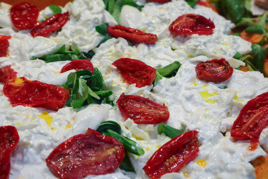 Delicious Italian gourmet pizza topped with fresh burrata cheese dried tomatoes and basil