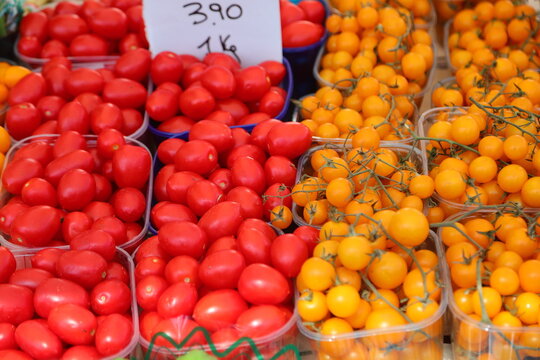 Fresh red and yellow cherry tomatoes displayed for sale in plastic trays at an Italian local farmers market stall