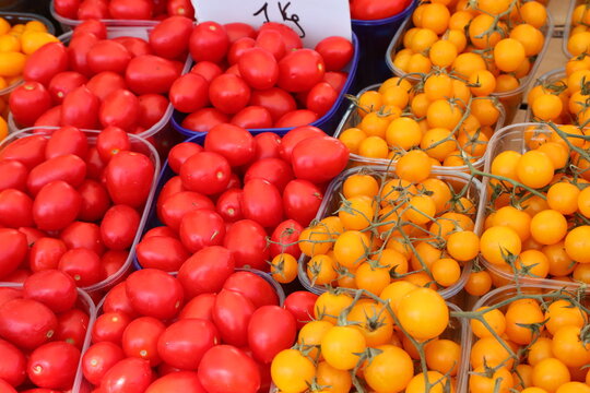 Fresh red and yellow cherry tomatoes displayed in plastic trays at market stall