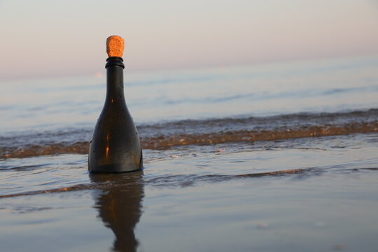Glass bottle with cork standing in wet sand on the beach shore at sunset