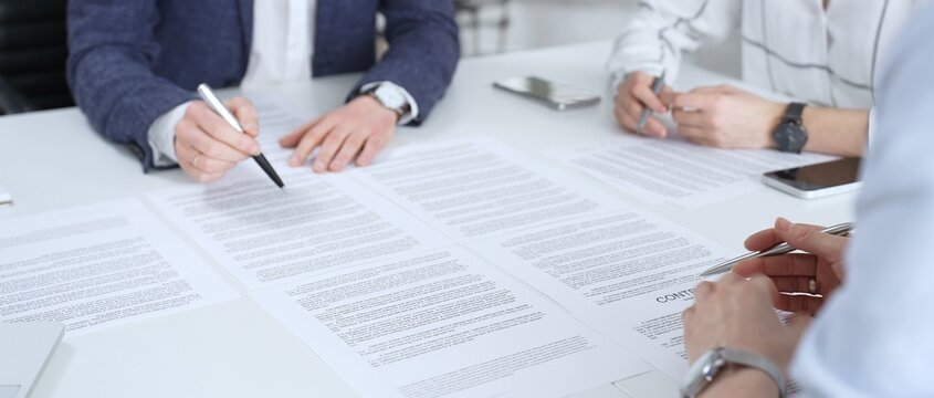 Professionals reviewing and signing contract documents across a white table, hands exchanging papers and pens to finalize negotiation, partnership and corporate agreement decisions