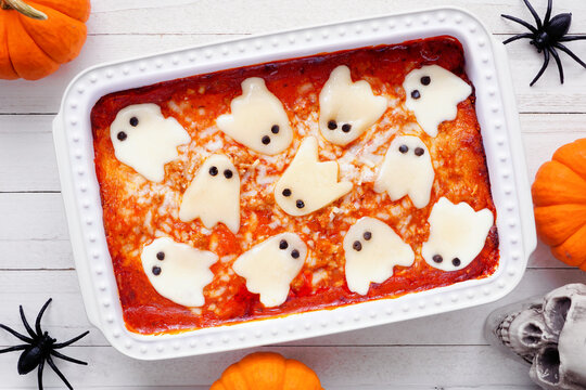 Halloween lasagna with spooky ghost cheese. Above view table scene on a white wood background.