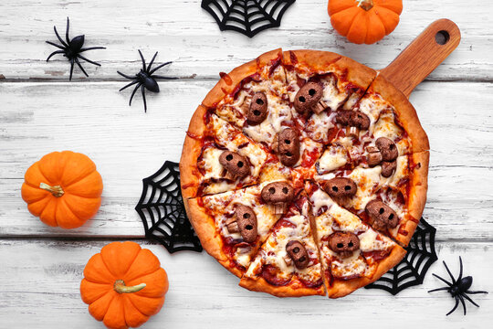 Halloween skull pizza. Above view table scene on a white wood background. Pepperoni and cheese with spooky mushroom skulls.