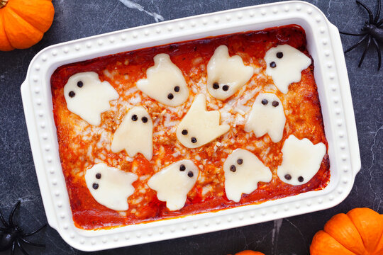 Halloween lasagna with spooky ghost cheese. Top down view table scene on a dark background.