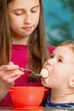 Young sister helping with childcare by feeding her little brother.