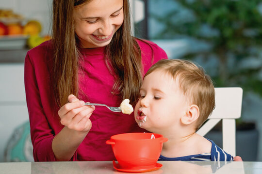 Caring older sibling helping a toddler eat his meal.