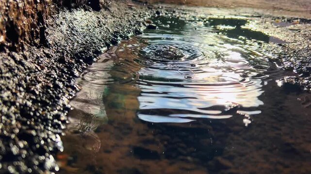 Large circular rain ripples spread across dark puddle near tunnel wall