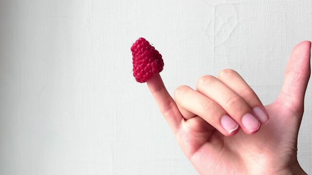 Two adult hands present a small raspberry between fingertips against wall