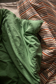 An unassembled bed in the bedroom, a blanket, and green and beige bedding.